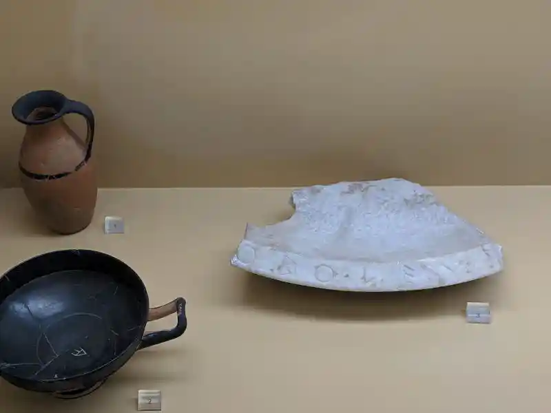 Group of artifacts for public use in ancient Athens, including a terracotta pitcher, a black-glazed cup, and a marble basin